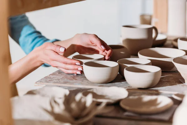 Cropped view of potter with ceramic bowls on shelves in workshop — Stock Photo