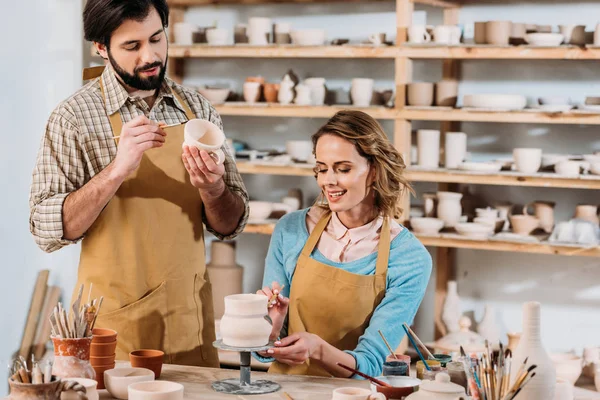 Happy potters painting ceramic dishware in workshop — Stock Photo