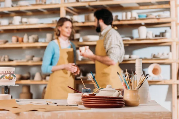 Selective focus of potters in workshop with ceramics and brushes on foreground — Stock Photo