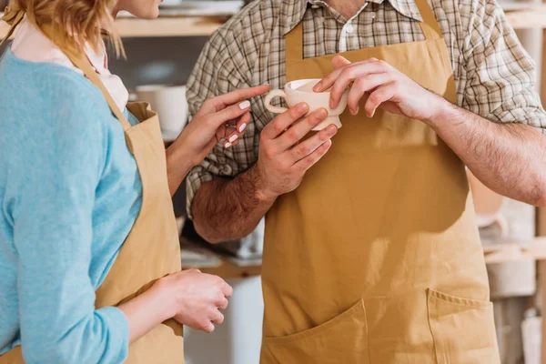 Cropped view of potters holding ceramic cup in workshop — Stock Photo