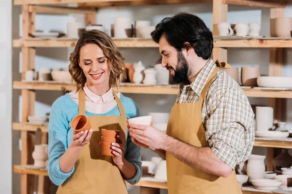 Happy potters holding ceramic dishware in workshop — Stock Photo