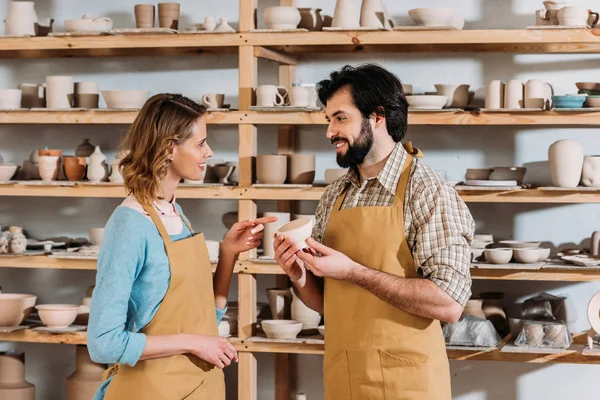 Lächelnde Töpfer reden und halten Keramikgeschirr in der Werkstatt — Stockfoto