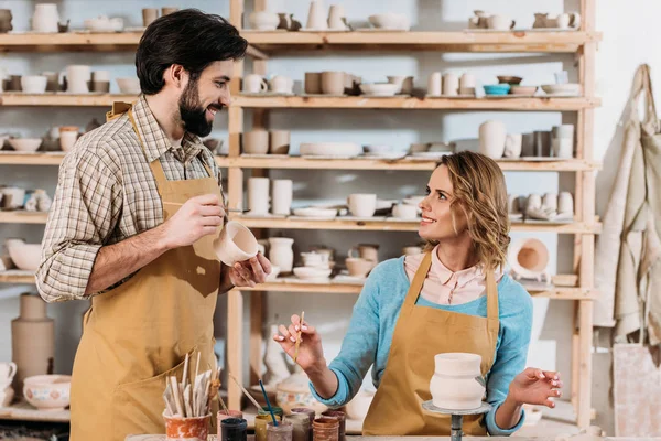 Alfareros sonrientes pintando vajilla de cerámica en taller - foto de stock