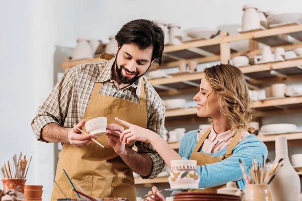 Couple of potters painting ceramic dishware in workshop — Stock Photo