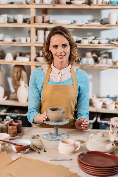 Happy female potter decorating ceramic bowl in workshop — Stock Photo