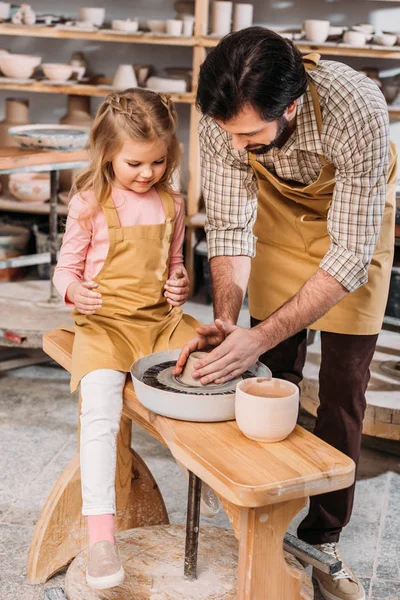 Padre enseñando a su hija a usar la rueda de cerámica en el taller - foto de stock