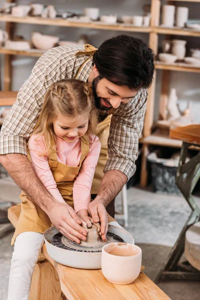 Happy daughter and father using pottery wheel in workshop — Stock Photo