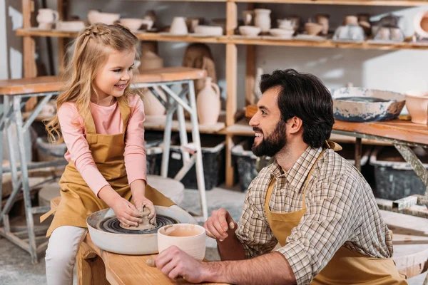 Happy kid making ceramic pot on pottery wheel with teacher in workshop — Stock Photo
