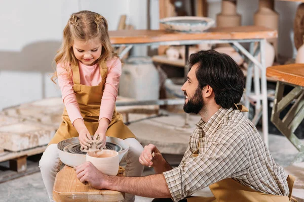 Adorable kid making ceramic pot on pottery wheel with teacher — Stock Photo