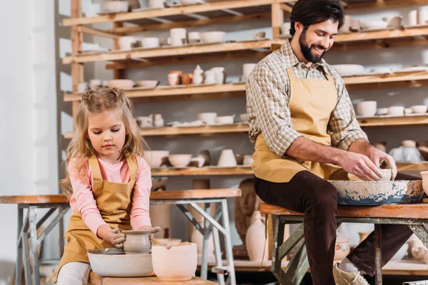 Niño haciendo olla de cerámica en la rueda de cerámica con el profesor cerca en el taller - foto de stock