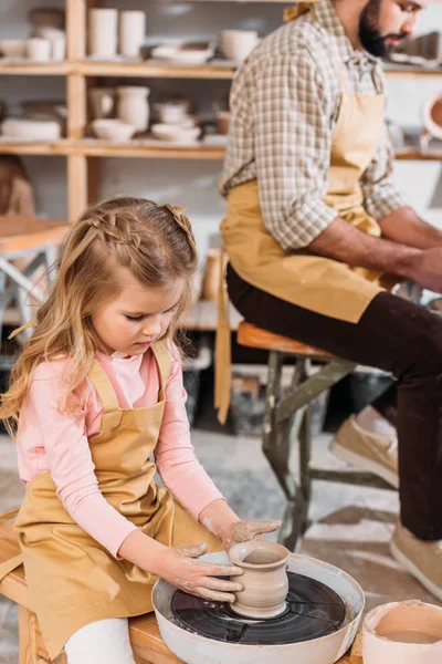 Child making ceramic pot on pottery wheel with teacher in workshop — Stock Photo