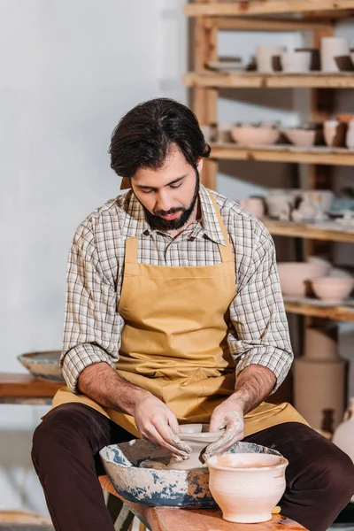 Бородатый гончар делает керамический горшок на гончарном круге в мастерской — стоковое фото