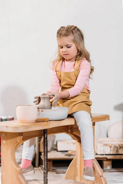 Niño rubio haciendo olla de cerámica en la rueda de cerámica en el taller - foto de stock