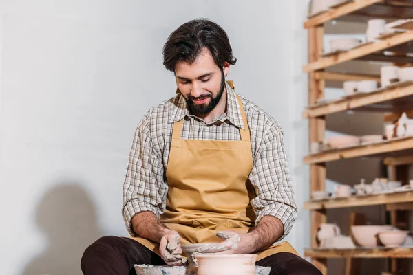 Hombre en delantal haciendo olla de cerámica en la rueda de cerámica en taller de cerámica - foto de stock