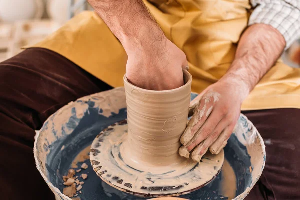 Vista recortada de alfarero haciendo olla de cerámica en la rueda de cerámica - foto de stock
