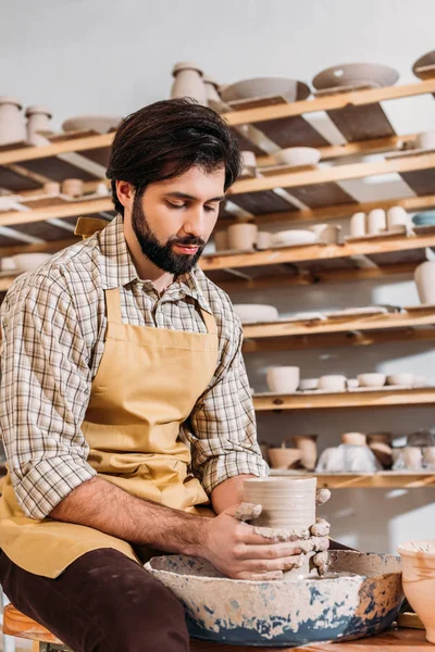 Potier barbu faisant vaisselle en céramique sur roue de poterie en atelier — Photo de stock