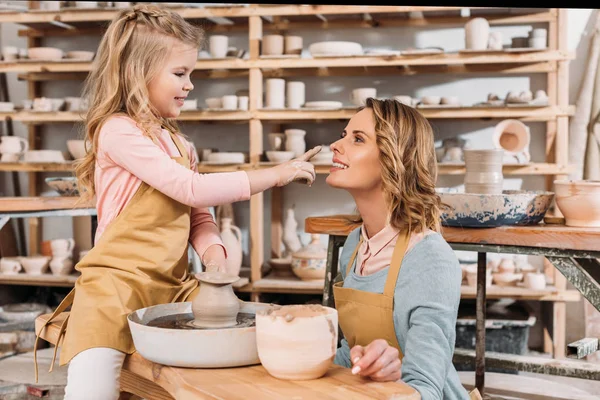 Adorable happy daughter touching nose of mother in pottery workshop — Stock Photo