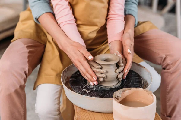 Vista recortada de maestro y niño haciendo olla de cerámica juntos en la rueda de cerámica - foto de stock