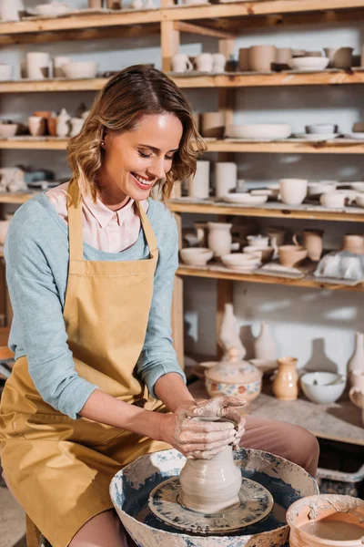 Potier féminin souriant faisant pot en céramique sur roue de poterie dans l'atelier — Photo de stock