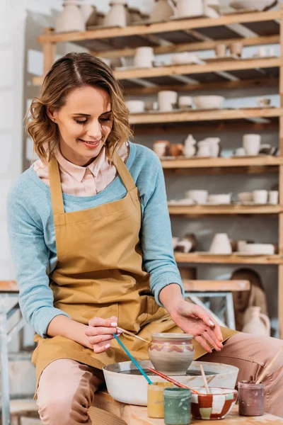 Lächelnde Frau bemalt Keramikgeschirr auf Töpferscheibe in Töpferei-Werkstatt — Stockfoto