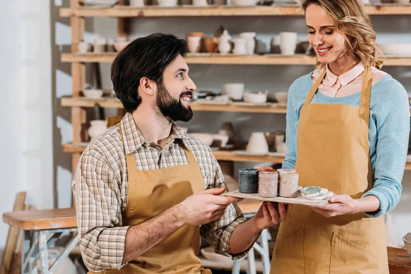 Smiling couple in aprons with paints in pottery workshop — Stock Photo