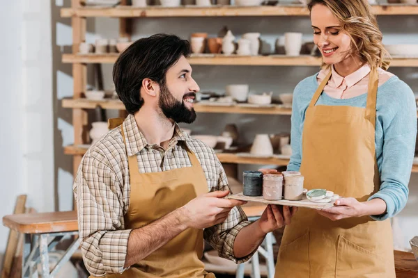 Coppia sorridente in grembiuli con vernici in laboratorio di ceramica — Foto stock