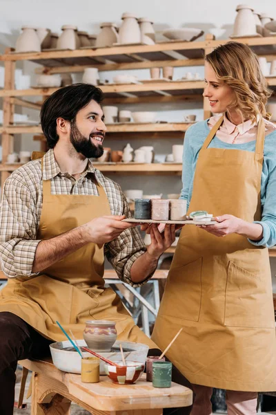 Pareja en delantales con pinturas en taller de cerámica - foto de stock