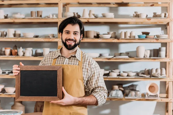 Bärtiger Mann mit Kreidetafel in Töpferwerkstatt mit Keramik — Stockfoto