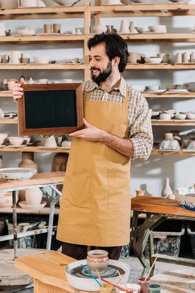 Sonriente propietario masculino sosteniendo pizarra en taller de cerámica - foto de stock