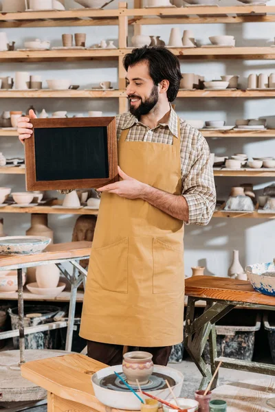 Lächelnder männlicher Besitzer mit Kreidetafel in Töpferwerkstatt — Stockfoto