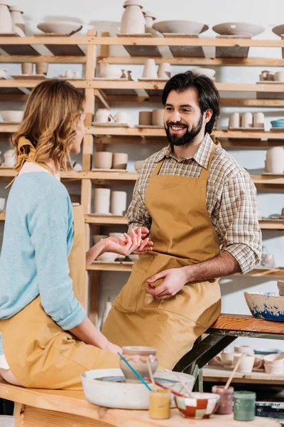 Happy couple in aprons with ceramics and paints in pottery workshop — Stock Photo