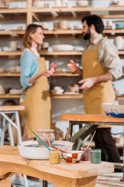 Selective focus of potters in workshop with paints on foreground — Stock Photo