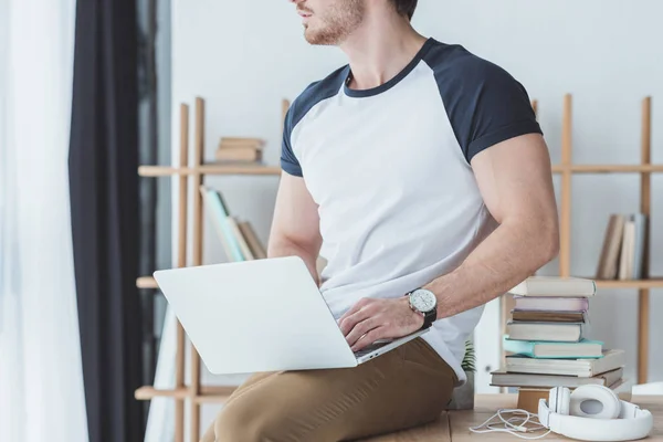 Обрізаний вид студента чоловічої статі з ноутбуком, що сидить на столі з навушниками — стокове фото