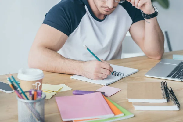 Vista recortada del estudiante masculino estudiando y escribiendo en copybook - foto de stock