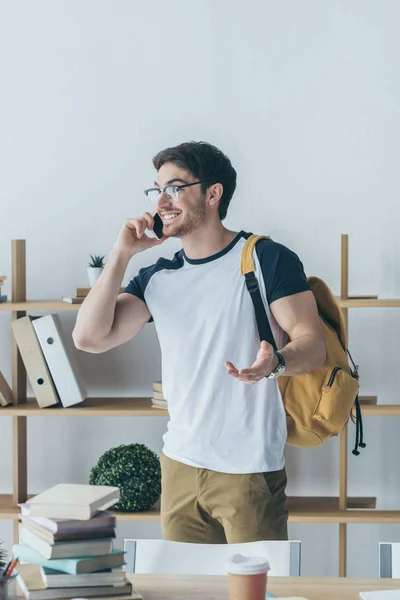Feliz estudiante masculino con mochila hablando en el teléfono inteligente - foto de stock