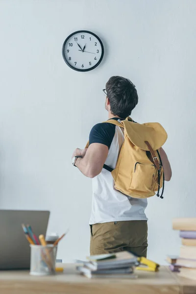 Rückansicht eines männlichen Studenten mit Rucksack, der auf die Uhr schaut — Stockfoto