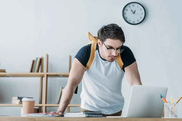 Handsome student with backpack using laptop — Stock Photo
