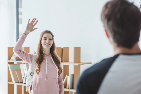 Selective focus of happy girl with backpack waving to her friend — Stock Photo