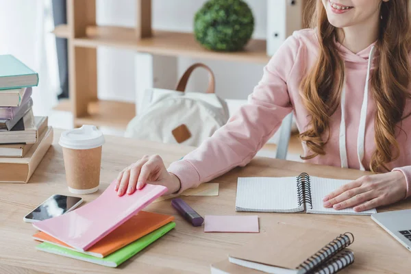 Vista recortada estudiante sonriente sentado en la mesa con copybooks - foto de stock