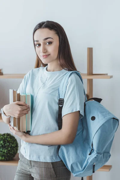 Hermosa chica de raza mixta con mochila celebración de libros - foto de stock