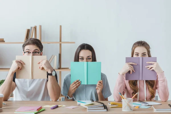 Tres jóvenes estudiantes sosteniendo libros mientras están sentados en la mesa - foto de stock