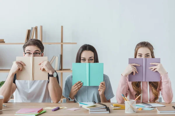 Tre giovani studenti che tengono libri mentre sono seduti a tavola — Foto stock