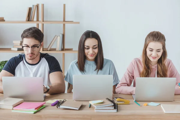 Estudantes multiétnicos usando laptops enquanto se sentam à mesa com livros — Fotografia de Stock