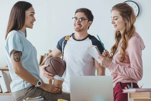 Молодые студенты сидят с баскетболом, кофе, чтобы пойти и ноутбук говорить вместе — стоковое фото