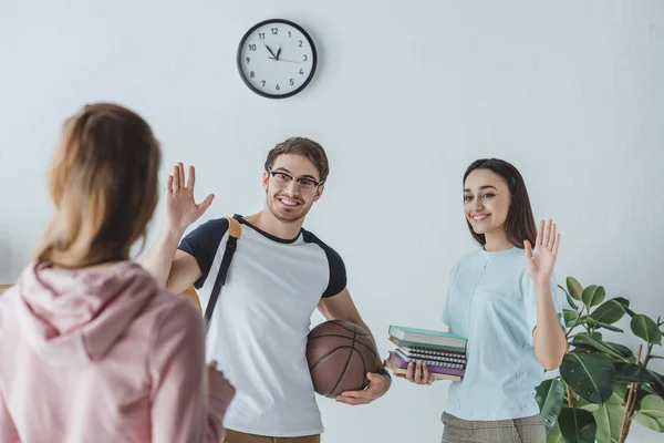 Jóvenes estudiantes con libros y baloncesto saludando a su amigo - foto de stock