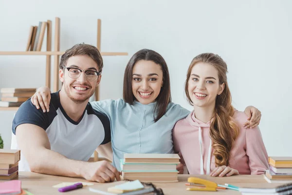 Young smiling students sitting at table with books — Stock Photo