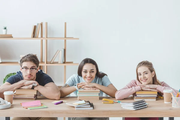 Jóvenes estudiantes multiculturales sentados a la mesa con libros y copybooks - foto de stock