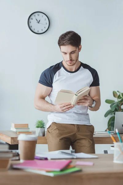 Estudiante masculino que estudia con libro en la habitación con copybooks - foto de stock