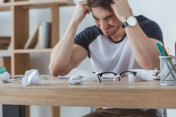 Depressed student studying at table with crumpled papers and eyeglasses — Stock Photo
