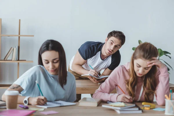 Junge Studenten schreiben Prüfung, während Mann abschreibt — Stockfoto